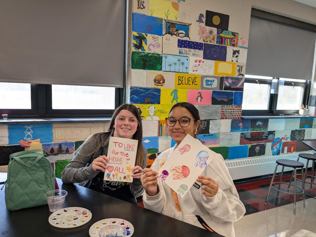 Sophomores Allison Centinaro and Nildali Ulerio proudly showcasing their watercolor paintings during a club meeting.